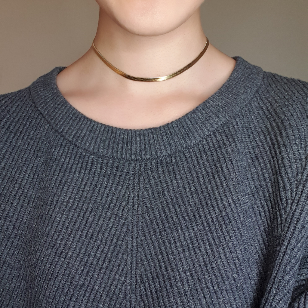 Gold flat lay snake necklace on model wearing grey jumper