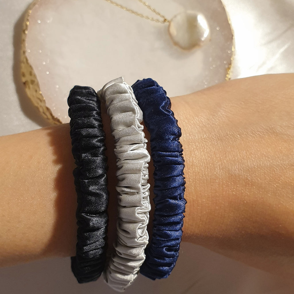 1 silver, 1 navy blue and 1 black slim silk scrunchie with pleats on model's arm